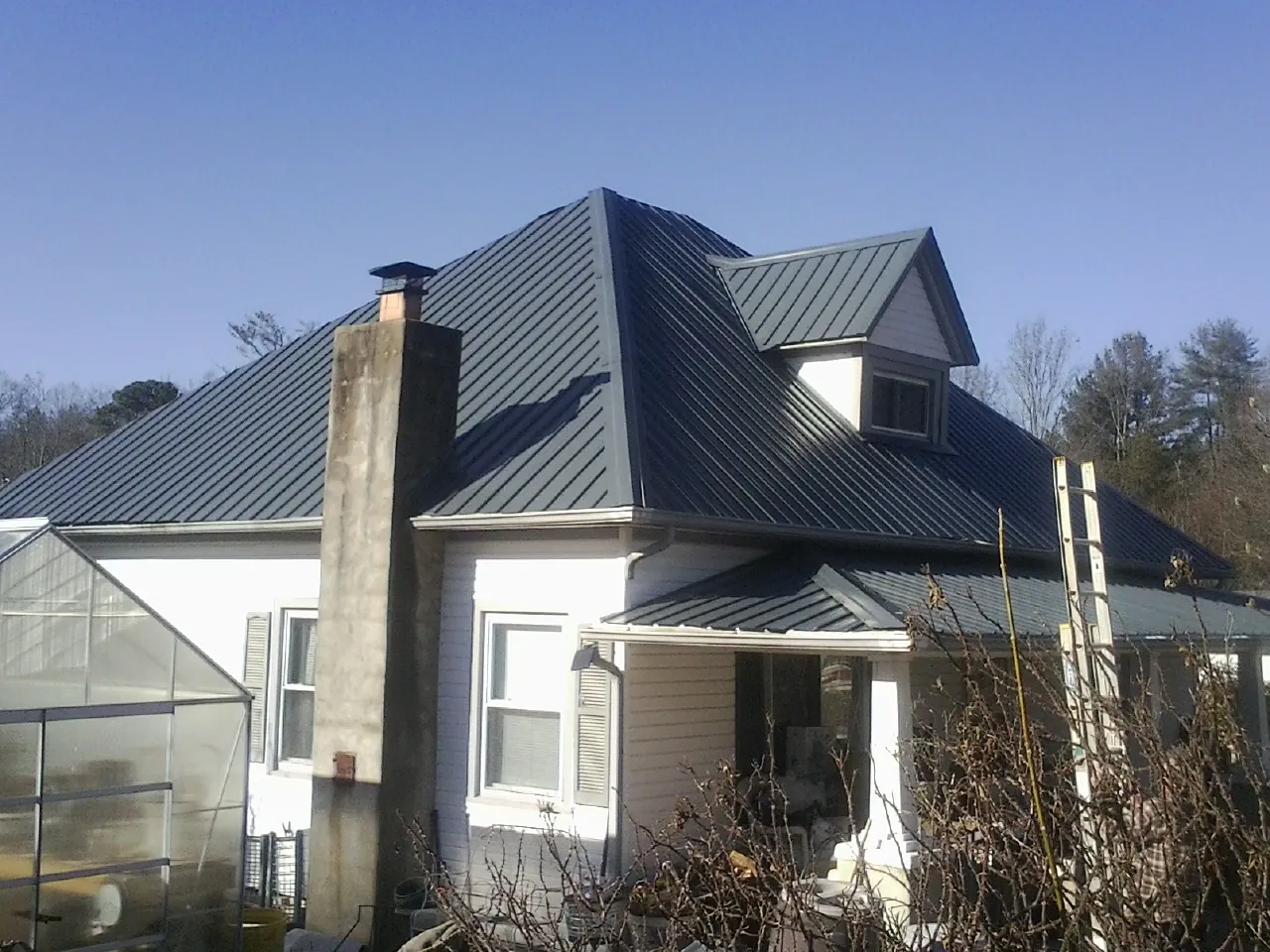 Dark blue standing seam metal roof on a white farmhouse with dormer — Slate & Tile Roof Repair by Roofing Brothers in Pico Rivera