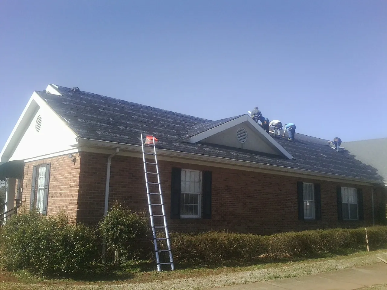 Crew tearing shingles off a brick ranch roof with a ladder set — Metal Roof Repair work by our crew in Pico Rivera