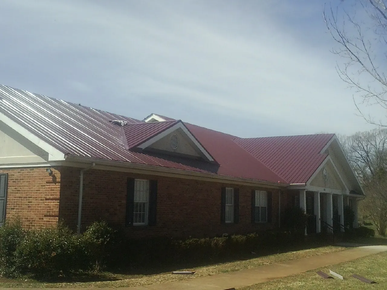 Red metal roof with gabled entries on a long brick building, from a Hail Damage Roof Repair job in Pico Rivera