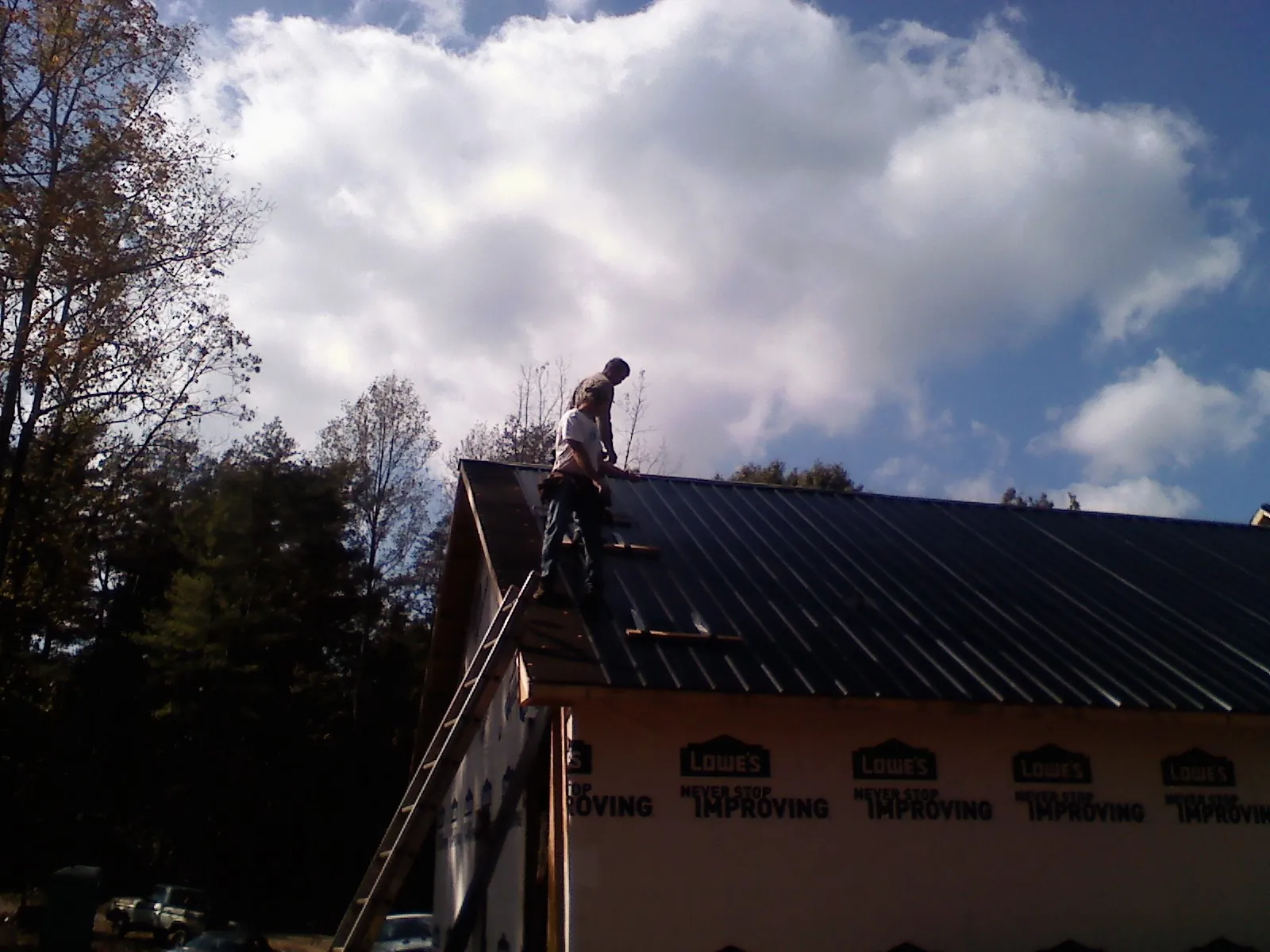 Roofer fastening dark metal panels high against a cloudy sky, from a Roof Inspection job in Pico Rivera